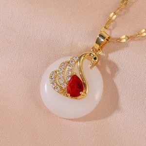 Golden swan necklace with red gemstone and white stone disc on orange silk background