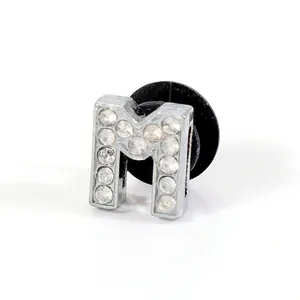 Macro shot of silver letter M shoe charm with sparkling rhinestones and black back plug
