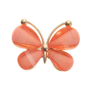 Detailed macro view of coral orange acrylic butterfly shoe charm with gold glitter and metal frame