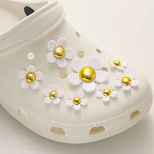 Close-up of white resin five-petal flower charms with gold centers on EVA garden clogs