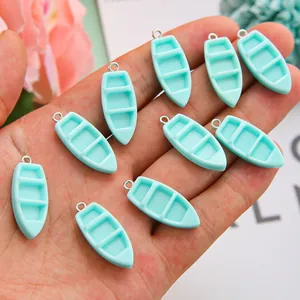 Detailopname van mintblauwe harsbootbedels in de hand voor DIY-sieraden en maatvergelijking