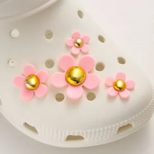 Close-up of pink resin flower shoe charms with gold centers on white clogs