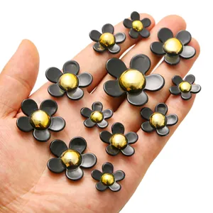 Detailed view of black and gold resin flower charms in three sizes held in a palm