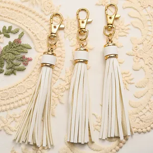 Detailed view of three white PU leather tassels with gold lobster clasps and lace background
