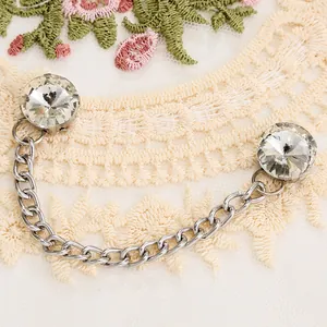 Détail d'une broche à double chaîne en métal argenté et strass sur tissu en dentelle