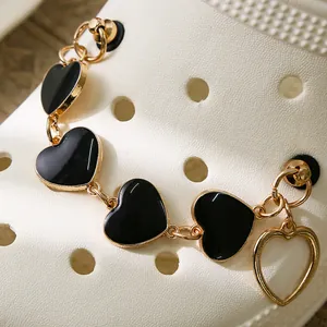 Détail de la chaîne de chaussure dorée avec cœurs en résine noire et pendentif cœur évidé