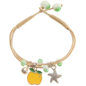 Detail of woven bracelet featuring yellow apple charm, metal star, and green beads