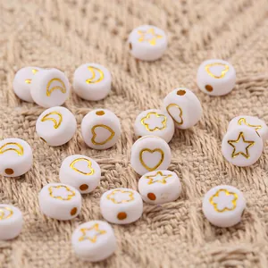 Macro shot of white acrylic beads with golden heart and star patterns on linen