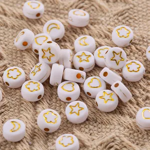 Close-up of white acrylic beads with gold stars hearts and moons on burlap texture