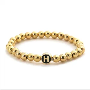 Detailed close-up of golden beaded stretch bracelet featuring a black letter H charm