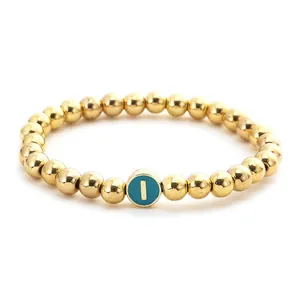 Detailed close-up of golden beaded bracelet featuring a teal enamel letter I charm