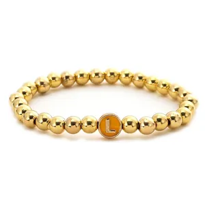 Close-up of golden beaded stretch bracelet featuring a yellow enamel round letter L charm