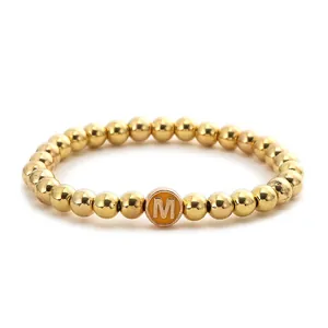 Detail of gold beaded stretch bracelet featuring a yellow round initial M charm