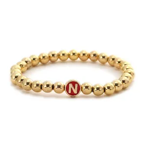 Detail of a beaded gold bracelet with a red enamel circular charm featuring the letter N