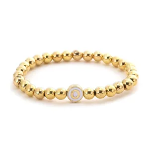 Close-up of golden beaded stretch bracelet featuring a white disc bead with letter O