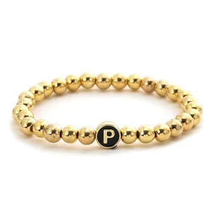 Detail of golden beaded elastic bracelet with a black circular letter P pendant
