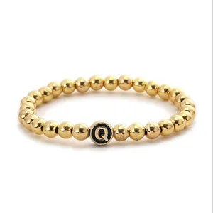 Detailed macro view of the golden bead bracelet featuring a black letter Q pendant charm