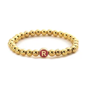Close-up of a golden beaded elastic bracelet with a pink cylindrical letter R charm