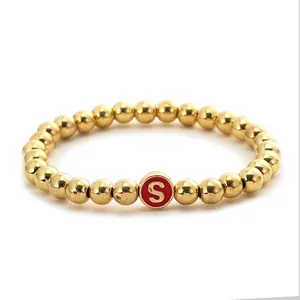 Detail of golden metal beaded elastic bracelet with a red round initial S charm pendant