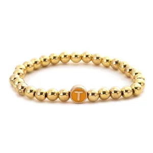 Detailed macro view of gold alloy beaded elastic bracelet with letter T charm