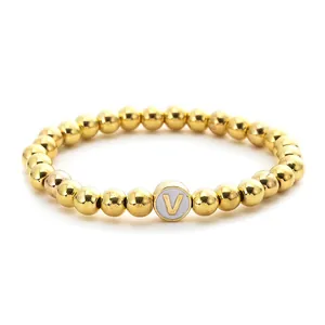 Detail of a gold beaded stretch bracelet featuring a round white charm with a golden letter V
