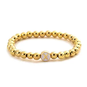 Detail of golden beaded elastic bracelet featuring a white round charm with letter X