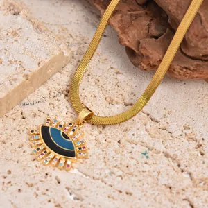 Gold evil eye pendant necklace with colorful zircons on a snake chain over rocks