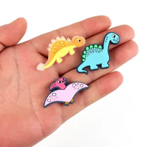 Drei farbenfrohe PVC Dinosaurier Schuhanhänger für Clogs in der Hand zur Größendarstellung
