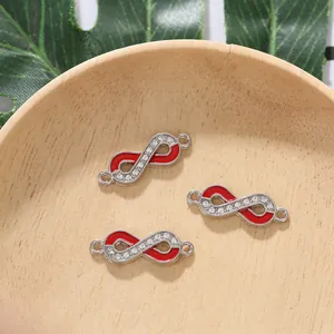 Three silver infinity charms with red enamel and crystals on a rustic wooden tray