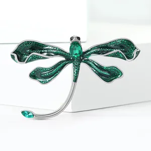 Macro detail of dragonfly brooch showing emerald green gemstones and silver metal wings