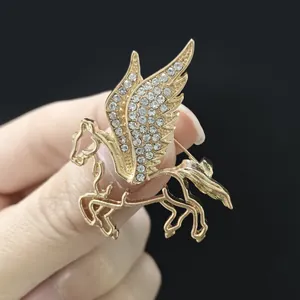 Dettaglio della spilla Pegasus dorata con ali di strass tenuta in mano