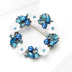 Détail macro d'une broche couronne de luxe avec cristaux bleus et fleurs en émail blanc