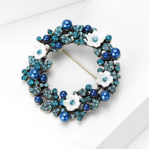 Makroansicht der blauen Strass-Kranzbrosche mit Perlen auf weißem geometrischem Ständer