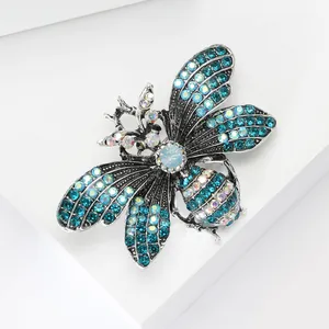 Detailed close-up of a silver bee brooch with blue and white rhinestones on white stands