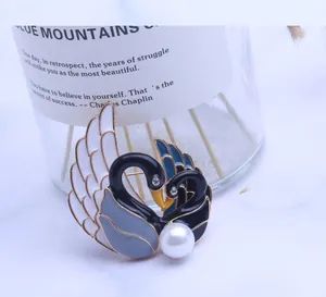 Detalle de broche de doble cisne en esmalte con perla y diseño de corazón