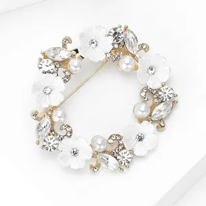 Détail d'une broche couronne dorée avec perles blanches et strass brillants sur blanc