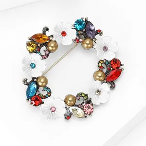 Vue macro d'une broche couronne florale vintage avec pierres colorées et perles champagne