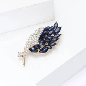Broche plume dorée avec gemmes marquises bleues et cristaux blancs sur support blanc
