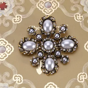 Detailed close-up of Baroque vintage cross brooch with grey pearls and white rhinestones