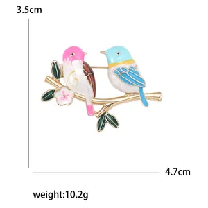 Cute bird brooch with colorful enamel on a golden branch with leaves and a small flower