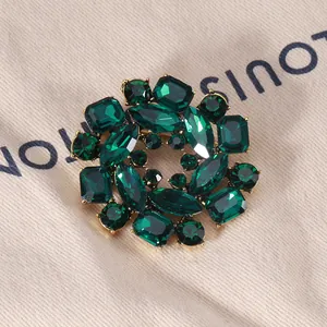 Detailed macro view of a vintage round wreath brooch with emerald green crystals and gold finish