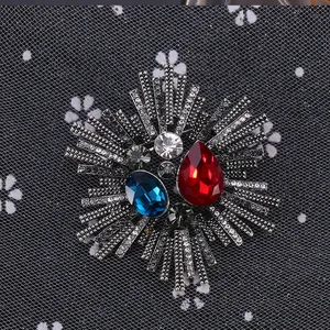 Detailed close-up of retro brooch with red teardrop stone and green crystal