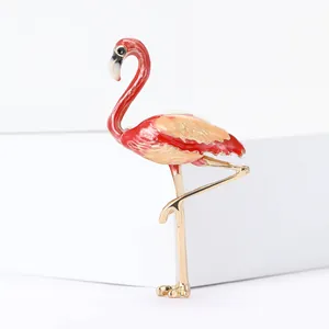 Détail macro d'une broche flamant rose en émail avec plumes rouges et finitions dorées