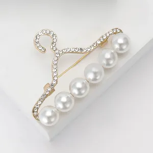 Détail de l'élégante broche cintre dorée avec perles blanches et strass scintillants
