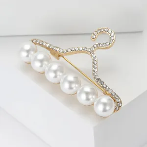Détail d'une broche cintre dorée avec perles blanches et strass sur support géométrique