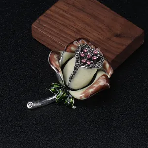 Dettaglio spilla rosa smaltata con strass a cuore su fondo nero materico e legno