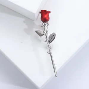Elegant red rose brooch with silver stem and two leaves on white geometric display