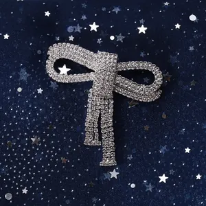 Macro shot of silver bow brooch with sparkling rhinestones and elegant tassels on blue fabric