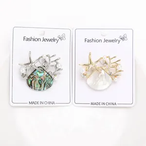 Vista de dos broches de perlas con conchas y estrellas de mar en tarjeta blanca