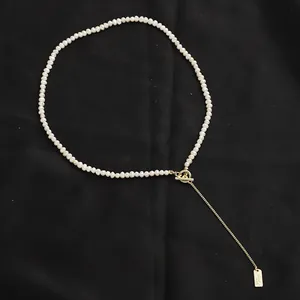Collana di perle bianche minimalista con chiusura a scatto OT dorata su sfondo nero